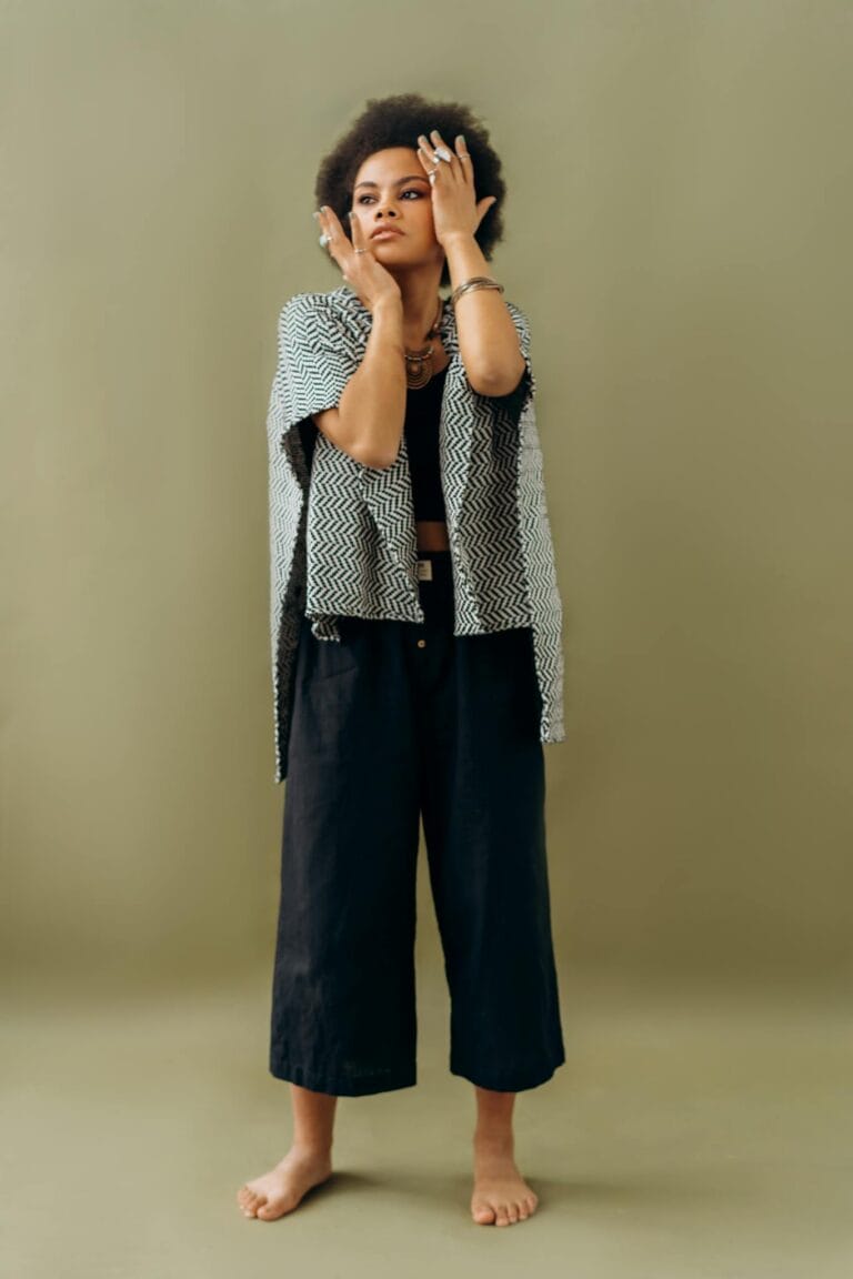 A fashionable woman poses confidently in modern attire against a plain backdrop.