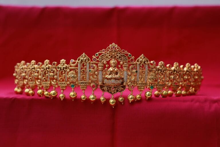 Intricately designed gold tiara featuring Buddha motifs on a vibrant red backdrop, symbolizing luxury and elegance.