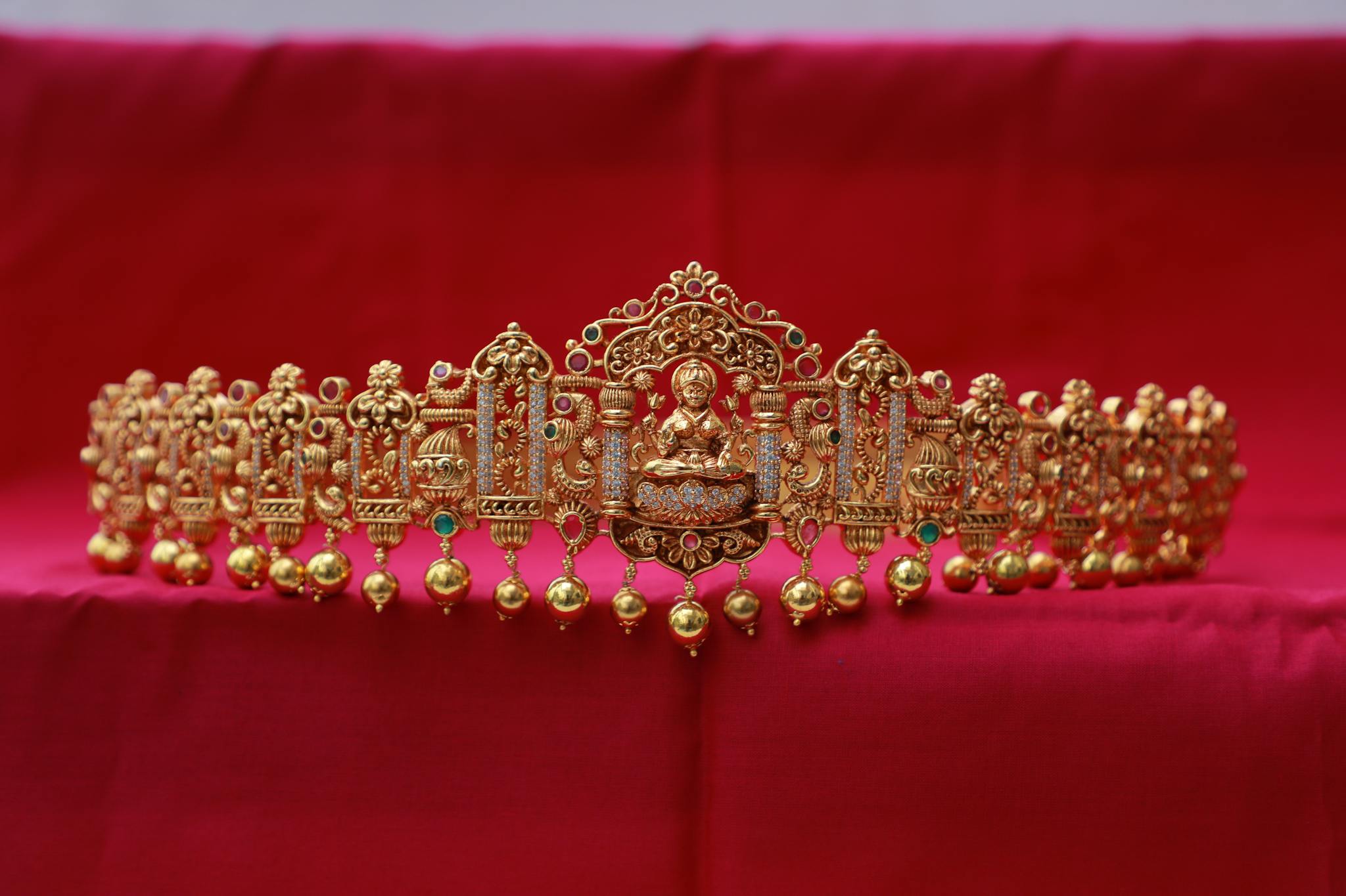 Intricately designed gold tiara featuring Buddha motifs on a vibrant red backdrop, symbolizing luxury and elegance.